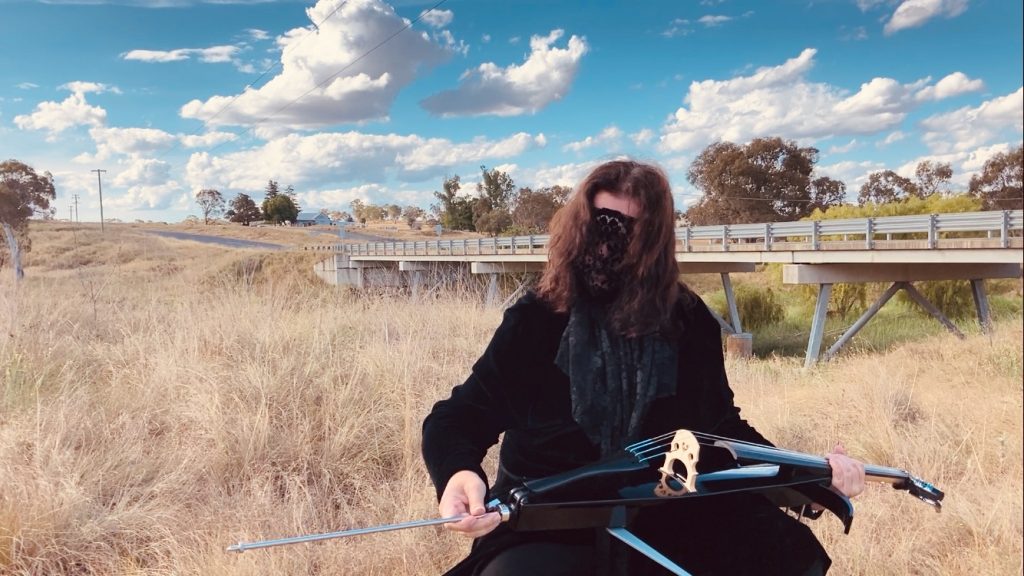 Laceface next to a bridge with her cello on Thunderbolts Way